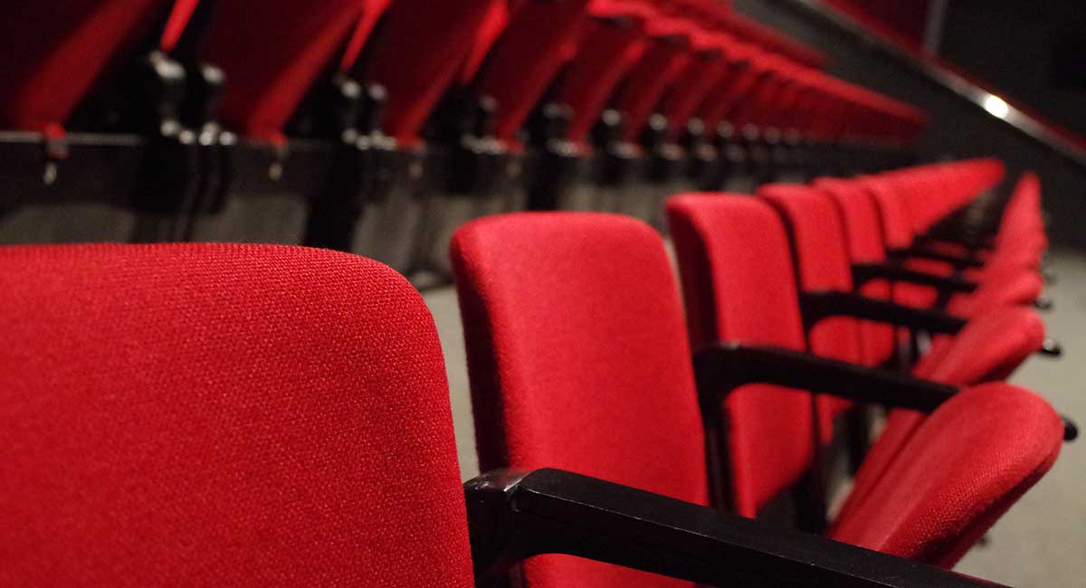 Reihen roter Sessel in einem Theatersaal.