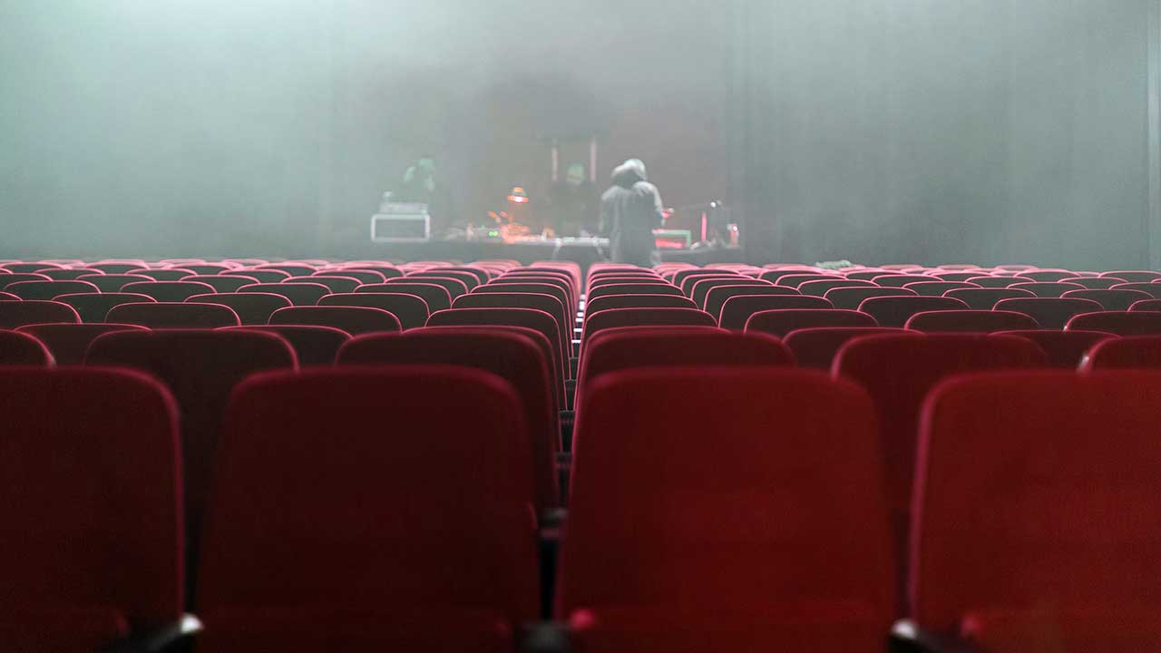 Leere Sitzreihen eines Theatersaales mit Blick auf die Bühne.