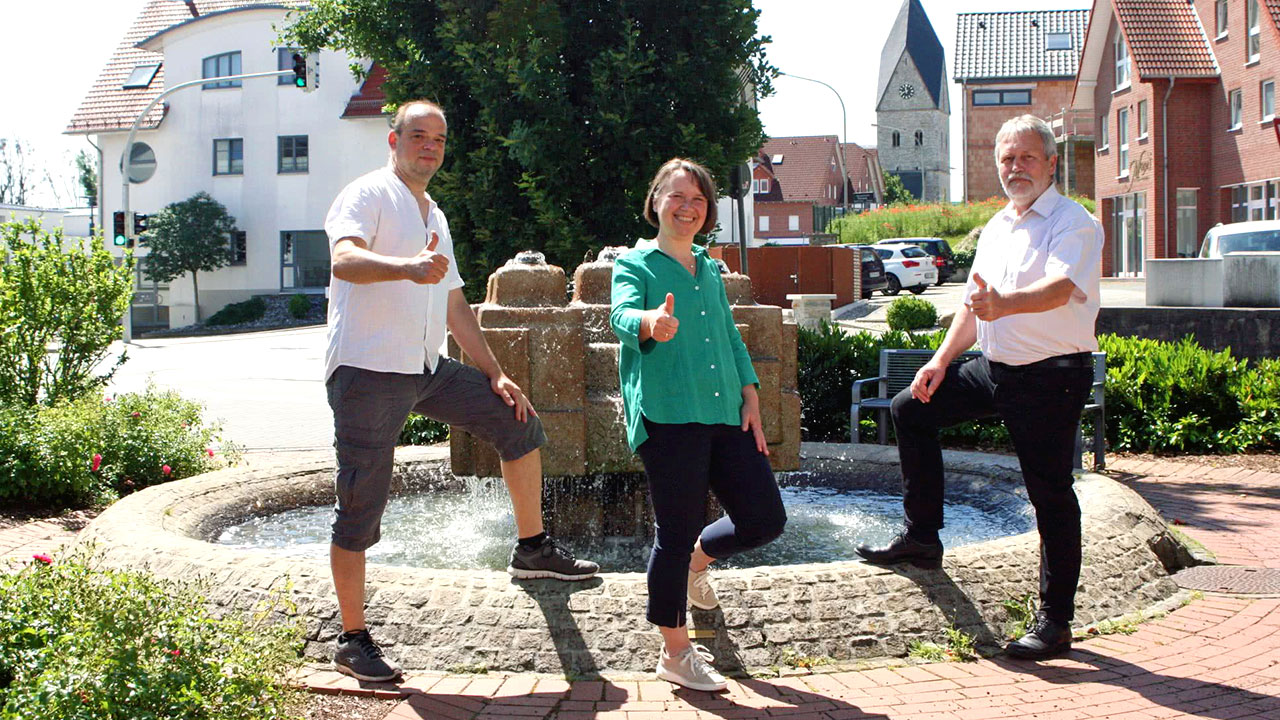 Drei Grüne Mitglieder des Dorfrates Wewer stehen vor dem Brunnen im Ortskern.