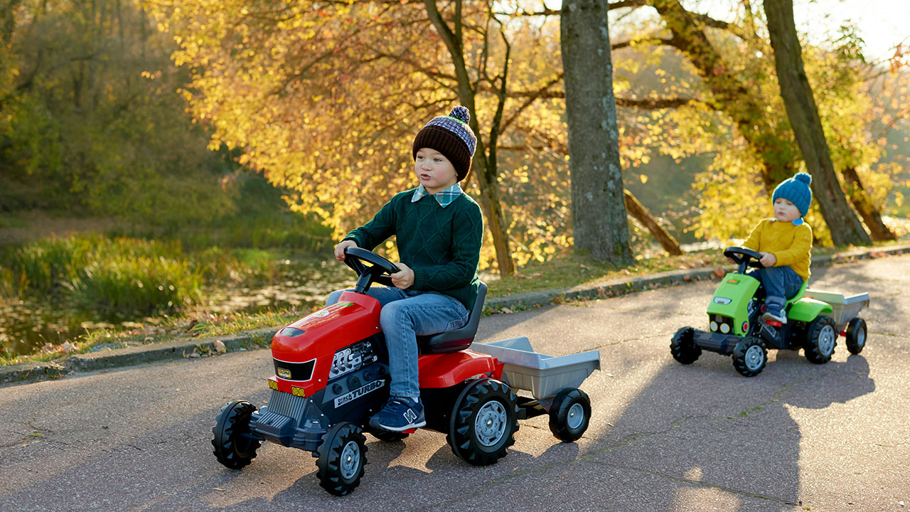 Zwei Kinder fahren auf ihren Spielzeugtreckern hintereinander her auf einer Straße.