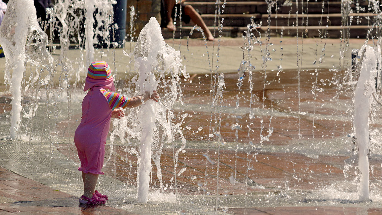 Ein kleines Mädchen kühlt sich an einem Springbrunnen ab.