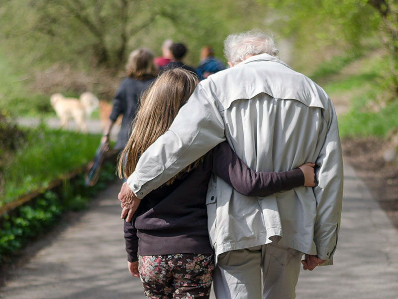 Eine Familie beim Spaziergang: Großvater und Enkeltochter gehen Arm in Arm.