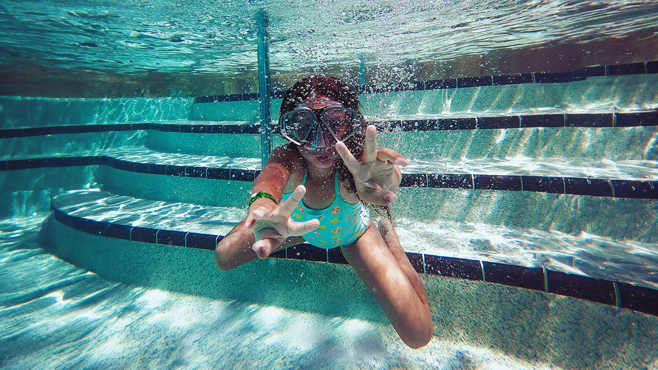 Ein Mädchen mit Taucherbrille taucht in einem Freibad.