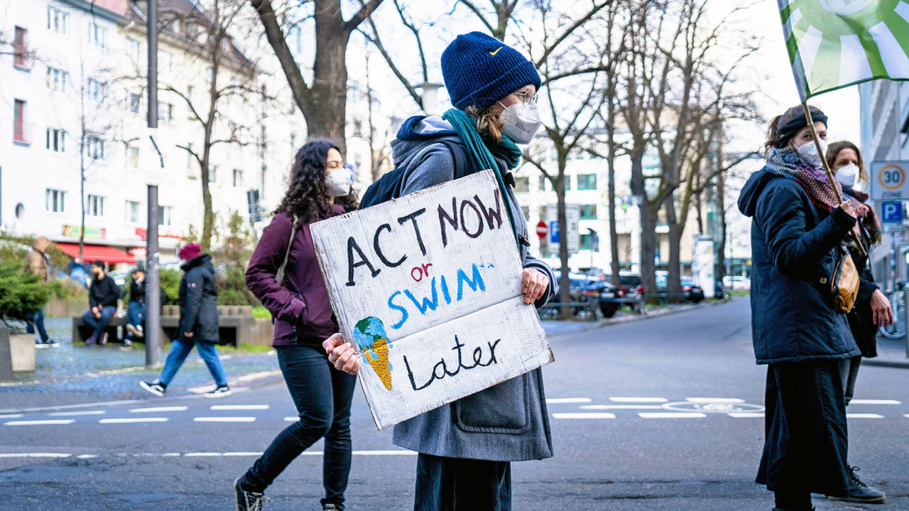 Eine Gruppe junger Frauen. Eine von Ihnen trägt das Schild „Act new or swim later“.