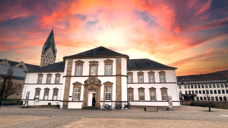 Vorderansicht der Stadtbibliothek Paderborn mit dramatischem Sonnenuntergangshimmel.